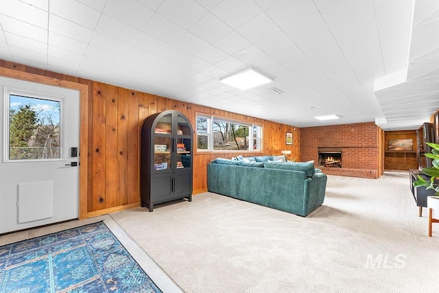 carpeted living room featuring a brick fireplace and wooden walls