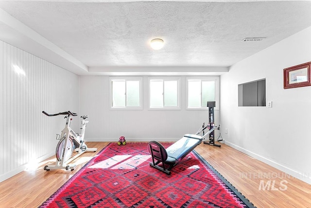 workout room featuring visible vents, a textured ceiling, baseboards, and wood finished floors