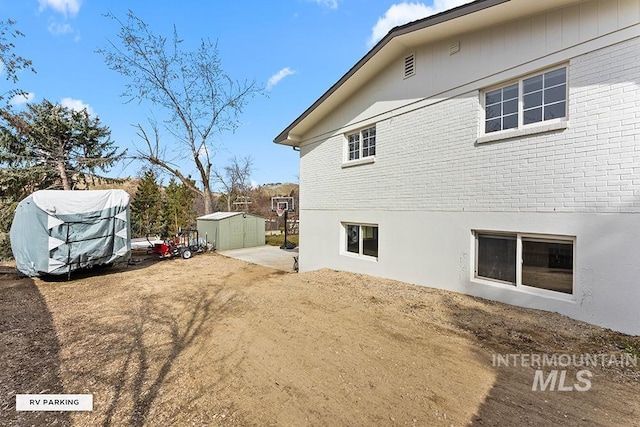 view of property exterior featuring dirt driveway, brick siding, an outdoor structure, and a storage shed