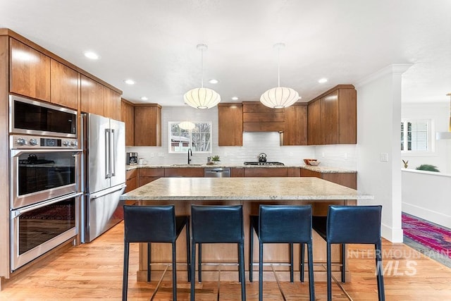 kitchen with appliances with stainless steel finishes, a breakfast bar, a sink, light wood-style floors, and backsplash