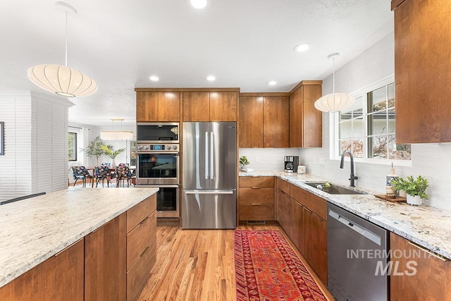 kitchen featuring light stone counters, brown cabinets, stainless steel appliances, a sink, and light wood-type flooring