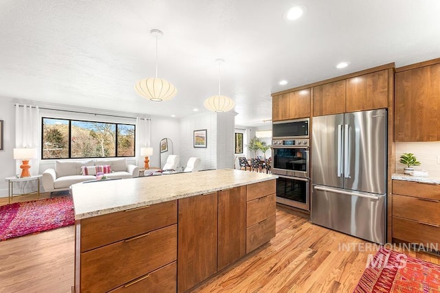 kitchen featuring light wood finished floors, appliances with stainless steel finishes, brown cabinets, open floor plan, and decorative light fixtures