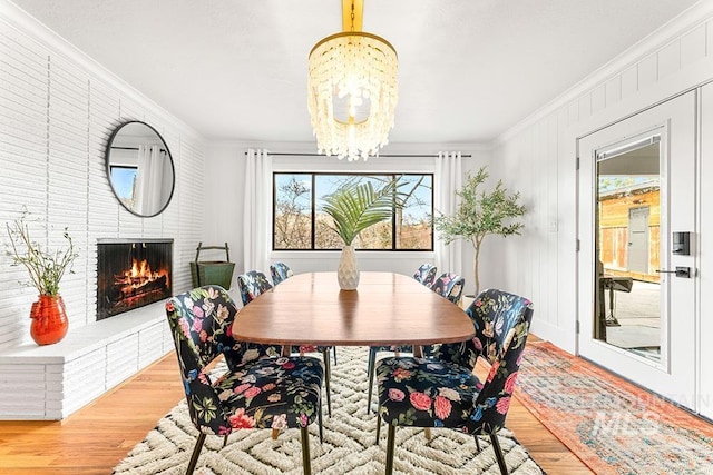 dining room featuring a chandelier, ornamental molding, a brick fireplace, and wood finished floors