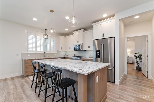 6009 W Riva Capri St, Meridian, ID 83646 - kitchen featuring light wood finished floors, stainless steel appliances, a kitchen island, a kitchen bar, and white cabinetry