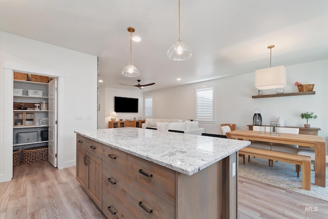 6009 W Riva Capri St, Meridian, ID 83646 - kitchen featuring light wood-style floors, ceiling fan, light stone countertops, a kitchen island, and hanging light fixtures