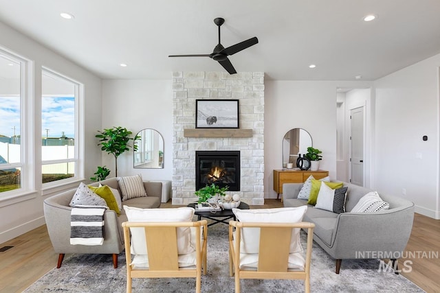 living room with light hardwood / wood-style floors, ceiling fan, and a stone fireplace