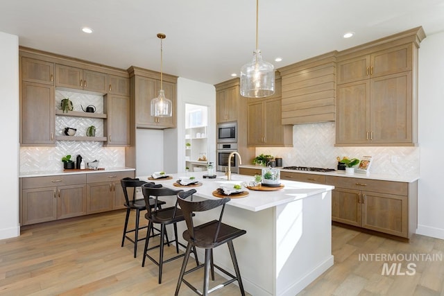 kitchen with appliances with stainless steel finishes, a breakfast bar, backsplash, light hardwood / wood-style flooring, and a center island with sink