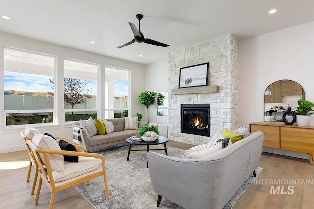 living room featuring ceiling fan, a stone fireplace, and light wood-type flooring