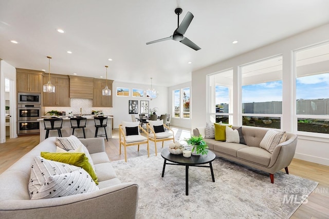 living room with ceiling fan with notable chandelier, light wood-type flooring, and sink