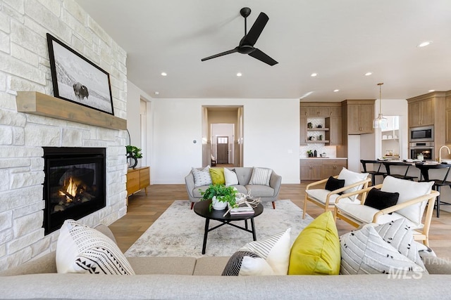 living room featuring light wood-type flooring, a fireplace, sink, and ceiling fan