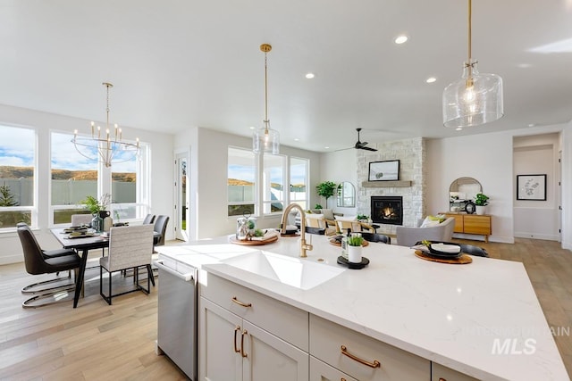 kitchen featuring pendant lighting, sink, light hardwood / wood-style flooring, a stone fireplace, and light stone countertops