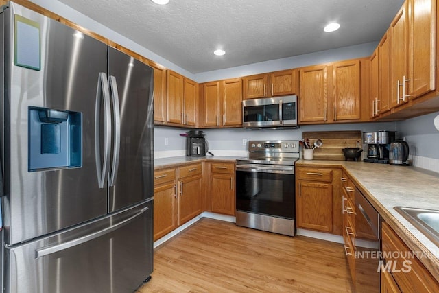 16042 N Saint Helens Dr, Nampa, ID 83651 - kitchen with light countertops, light wood finished floors, brown cabinetry, and appliances with stainless steel finishes