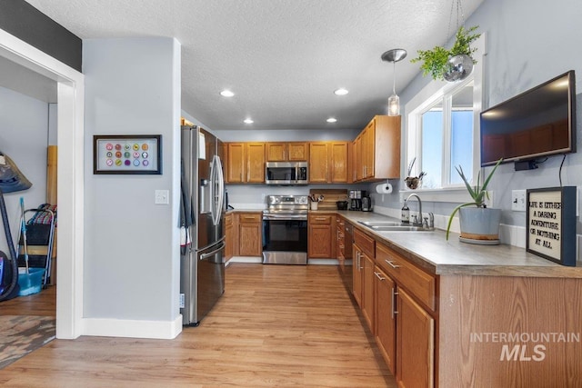 16042 N Saint Helens Dr, Nampa, ID 83651 - kitchen with brown cabinets, a sink, light wood-type flooring, a textured ceiling, and appliances with stainless steel finishes