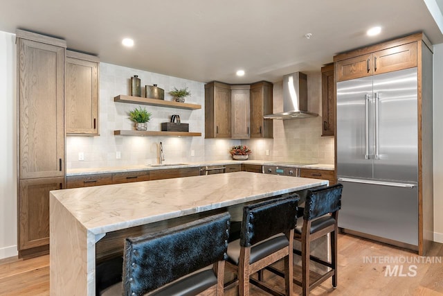 kitchen with stainless steel built in refrigerator, sink, a center island, and wall chimney range hood