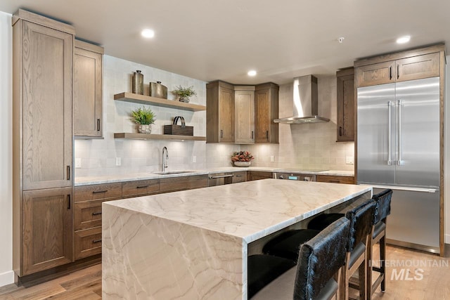 kitchen with wall chimney exhaust hood, sink, appliances with stainless steel finishes, a kitchen breakfast bar, and a kitchen island