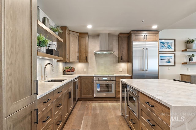 kitchen featuring wall chimney range hood, sink, backsplash, built in appliances, and light wood-type flooring