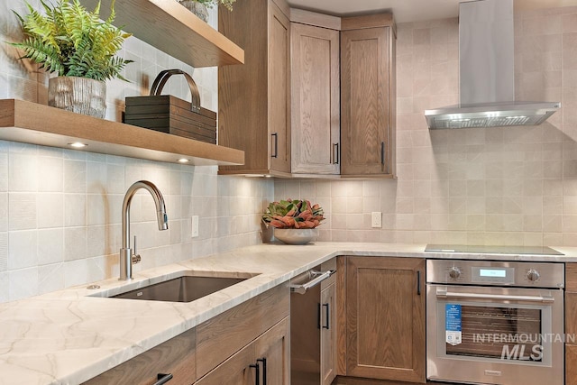 kitchen with wall chimney range hood, sink, backsplash, light stone countertops, and stainless steel oven