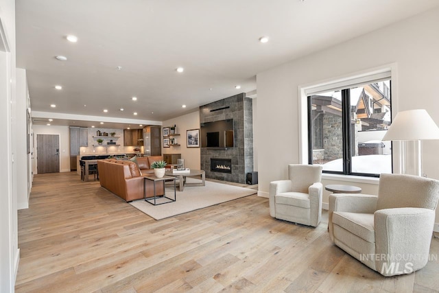 living room with a tiled fireplace and light wood-type flooring