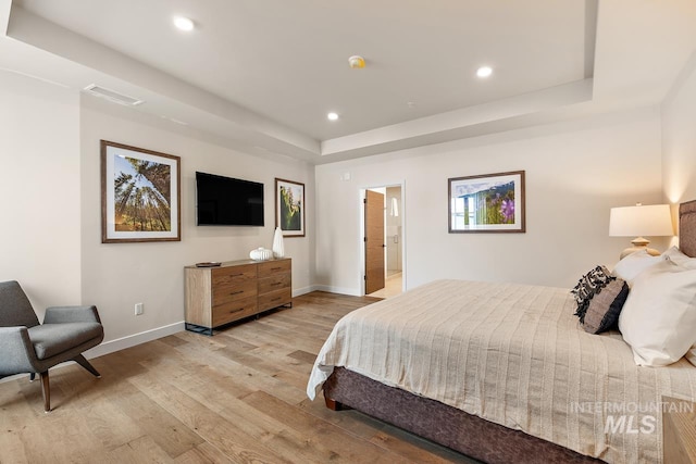 bedroom with light hardwood / wood-style floors and a tray ceiling