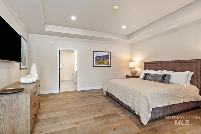 bedroom featuring ensuite bathroom, light wood-type flooring, and a tray ceiling