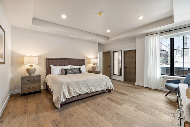 bedroom with a raised ceiling and light hardwood / wood-style flooring