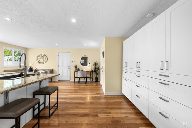 kitchen featuring a sink, a kitchen breakfast bar, a textured ceiling, and wood finished floors