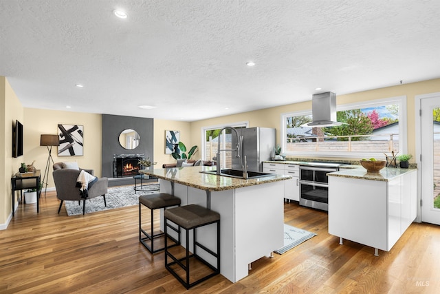 kitchen featuring double oven range, a textured ceiling, island exhaust hood, freestanding refrigerator, and a breakfast bar