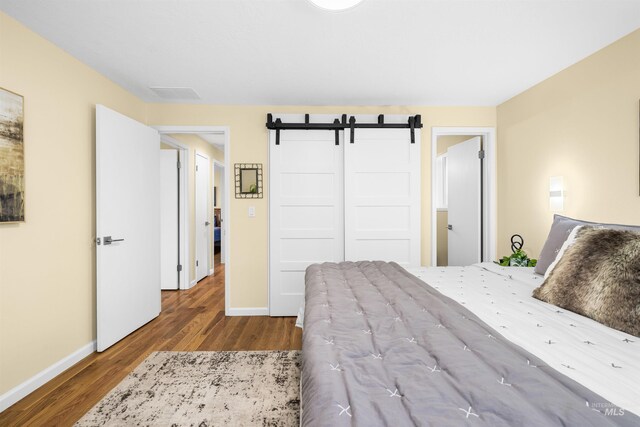 bedroom with baseboards, a closet, wood finished floors, and visible vents