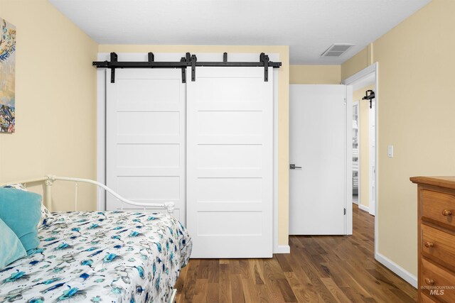 bedroom featuring baseboards, visible vents, a barn door, and dark wood finished floors