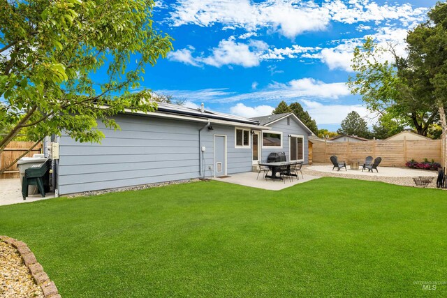 back of property with a lawn, a fenced backyard, a patio area, and solar panels