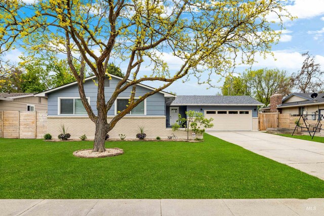 split level home featuring a garage, fence, a front yard, brick siding, and driveway