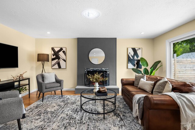living room featuring a textured ceiling, a large fireplace, wood finished floors, baseboards, and recessed lighting