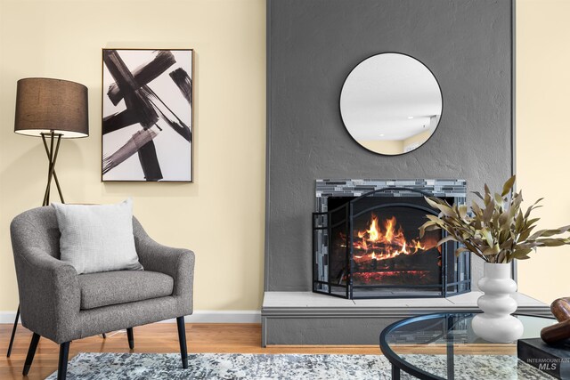 sitting room featuring baseboards, a lit fireplace, and wood finished floors
