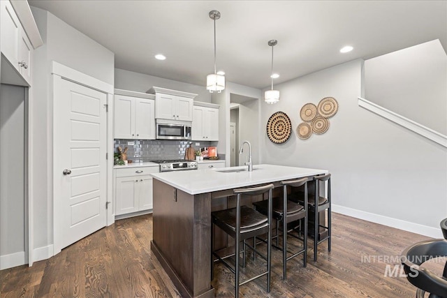 kitchen with backsplash, stainless steel appliances, a kitchen island with sink, decorative light fixtures, and white cabinets