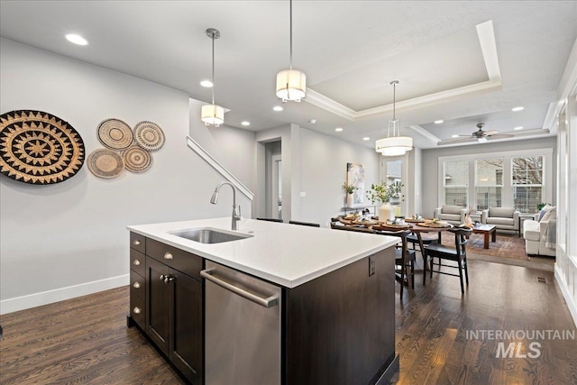 kitchen featuring stainless steel dishwasher, a raised ceiling, ceiling fan, a kitchen island with sink, and sink