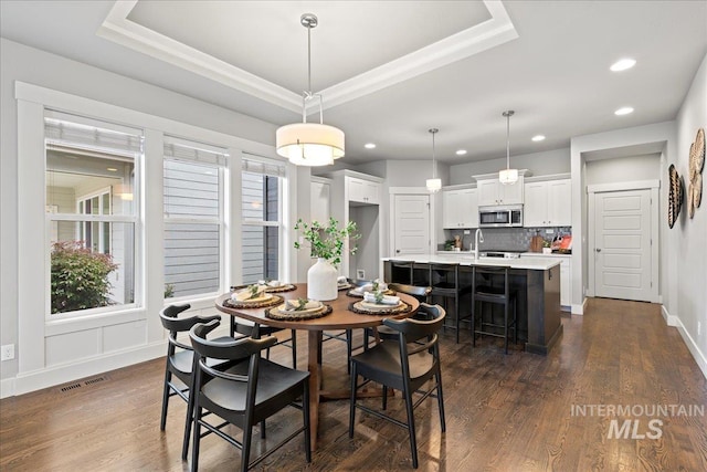 dining space featuring a raised ceiling, dark hardwood / wood-style flooring, and sink