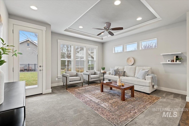 carpeted living room featuring plenty of natural light, ceiling fan, and a raised ceiling