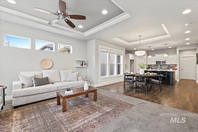 living room with a raised ceiling, a wealth of natural light, ceiling fan, and dark hardwood / wood-style flooring