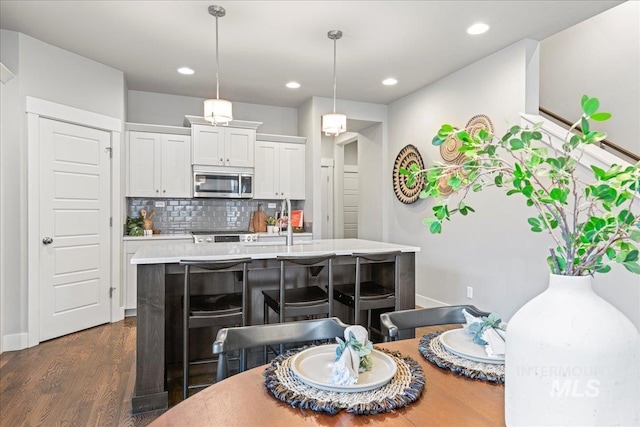 kitchen featuring white cabinetry, hanging light fixtures, tasteful backsplash, an island with sink, and a breakfast bar