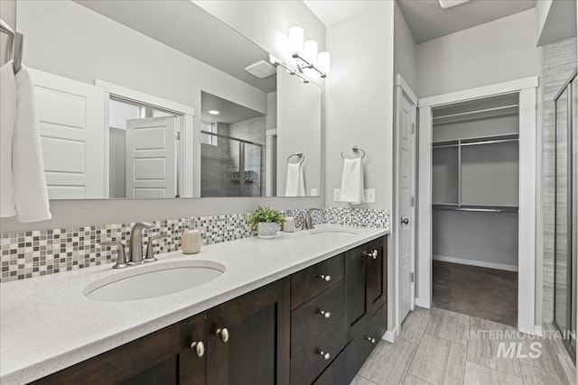 bathroom featuring vanity, a shower with shower door, and backsplash