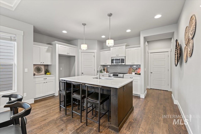 kitchen featuring sink, stainless steel appliances, backsplash, a kitchen island with sink, and white cabinets