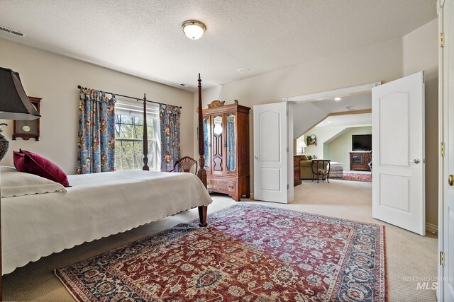bedroom featuring visible vents, a textured ceiling, and light carpet