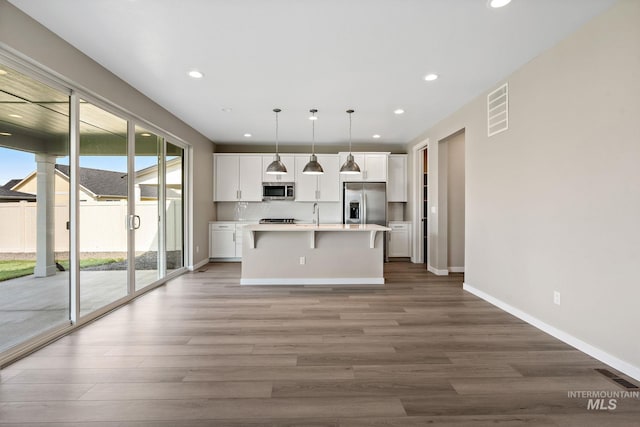 kitchen with visible vents, a center island with sink, wood finished floors, stainless steel appliances, and white cabinets