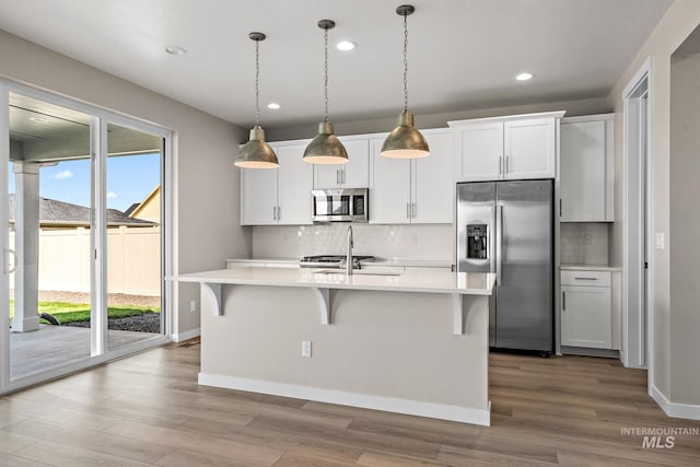 kitchen with a kitchen island with sink, a sink, stainless steel appliances, light countertops, and a kitchen bar