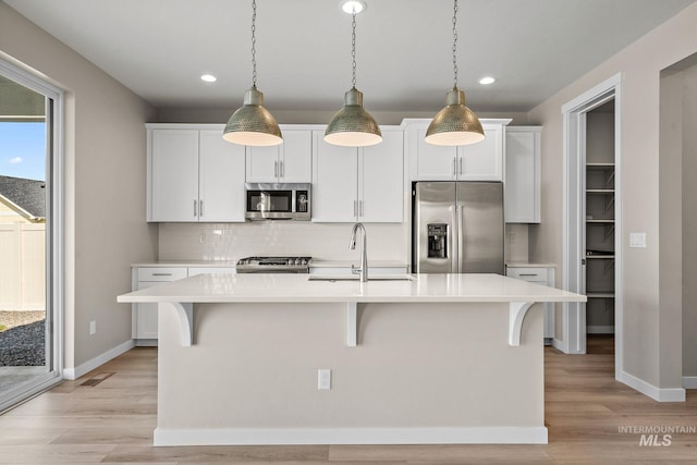 kitchen with a center island with sink, light countertops, decorative backsplash, stainless steel appliances, and a sink