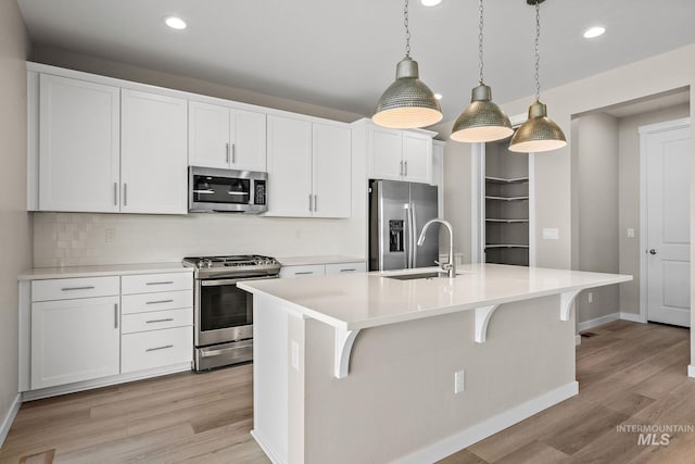 kitchen featuring an island with sink, a sink, stainless steel appliances, light wood-style floors, and light countertops