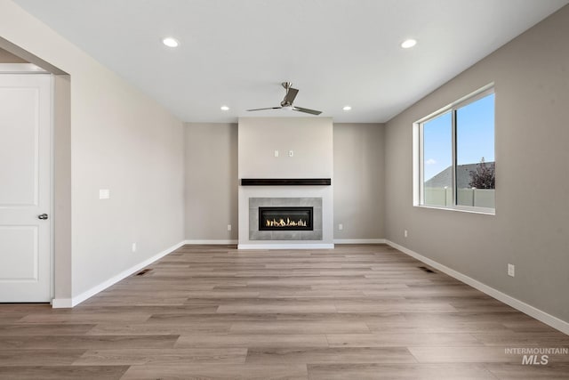 unfurnished living room with light wood finished floors, visible vents, baseboards, a tiled fireplace, and recessed lighting