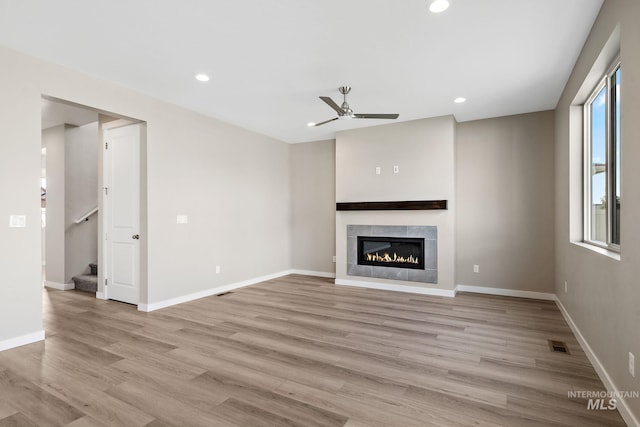 unfurnished living room with visible vents, light wood-style flooring, a tiled fireplace, recessed lighting, and stairway