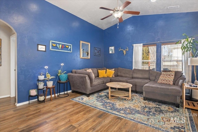 living room featuring arched walkways, visible vents, vaulted ceiling, wood finished floors, and baseboards