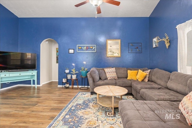 living area featuring baseboards, arched walkways, a ceiling fan, wood finished floors, and a textured ceiling